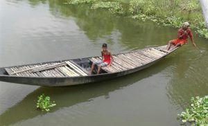 Two boys sail a boat on a polluted stretch of Mathabhanga river